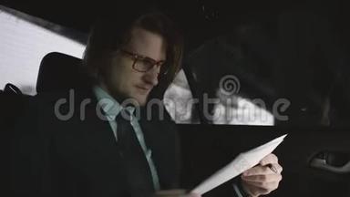 漂亮的男人，棕色头发，穿着开心果衬衫，灰色西装，戴着眼镜，坐在车里看文件